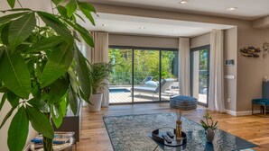 A spacious living room with a large potted plant, a glass coffee table, and a view of an outdoor deck. - VILLA GRAZIELLA 200 M FROM THE BEACH (Èze)
