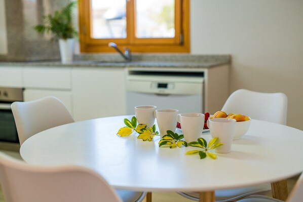 A round white table with four white cups and a bowl of fruit.