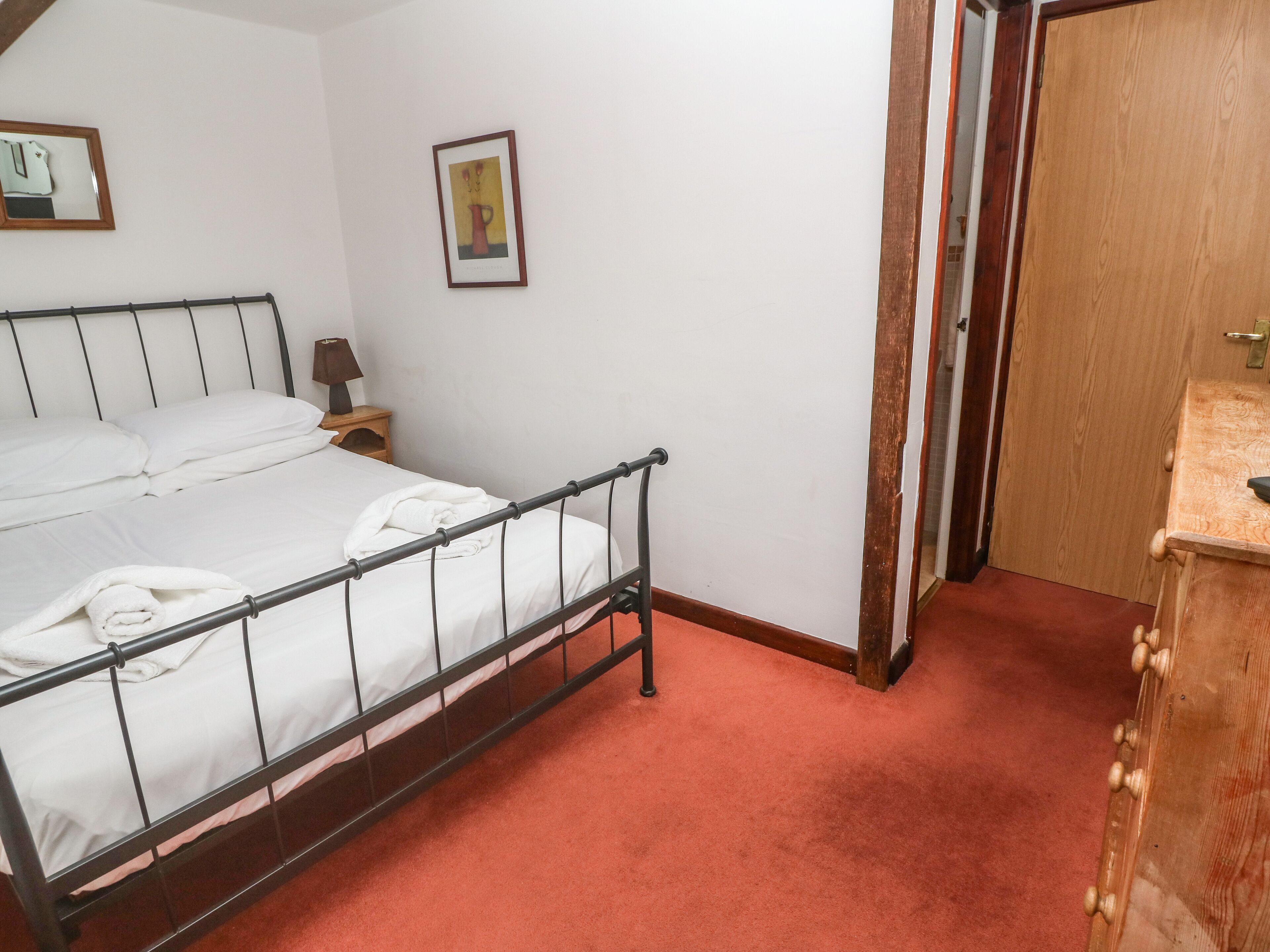 A neatly made bed with white linens, a bedside table with a lamp, and a framed picture on the wall.