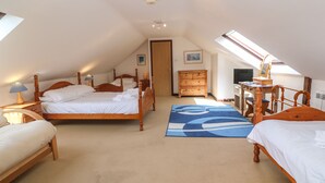 A bedroom with a sloped ceiling, a wooden bed, a dresser, a desk with a computer, and a large window. - Barn Cottage (Penzance)