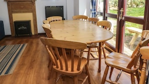 Zona pranzo con tavolo e sedie in legno, camino, televisione e vista sull'esterno tramite ampie finestre.