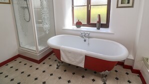 A bathroom with a freestanding bathtub, a glass shower enclosure, and a window with a view of greenery. - Barn Cottage (Penzance)