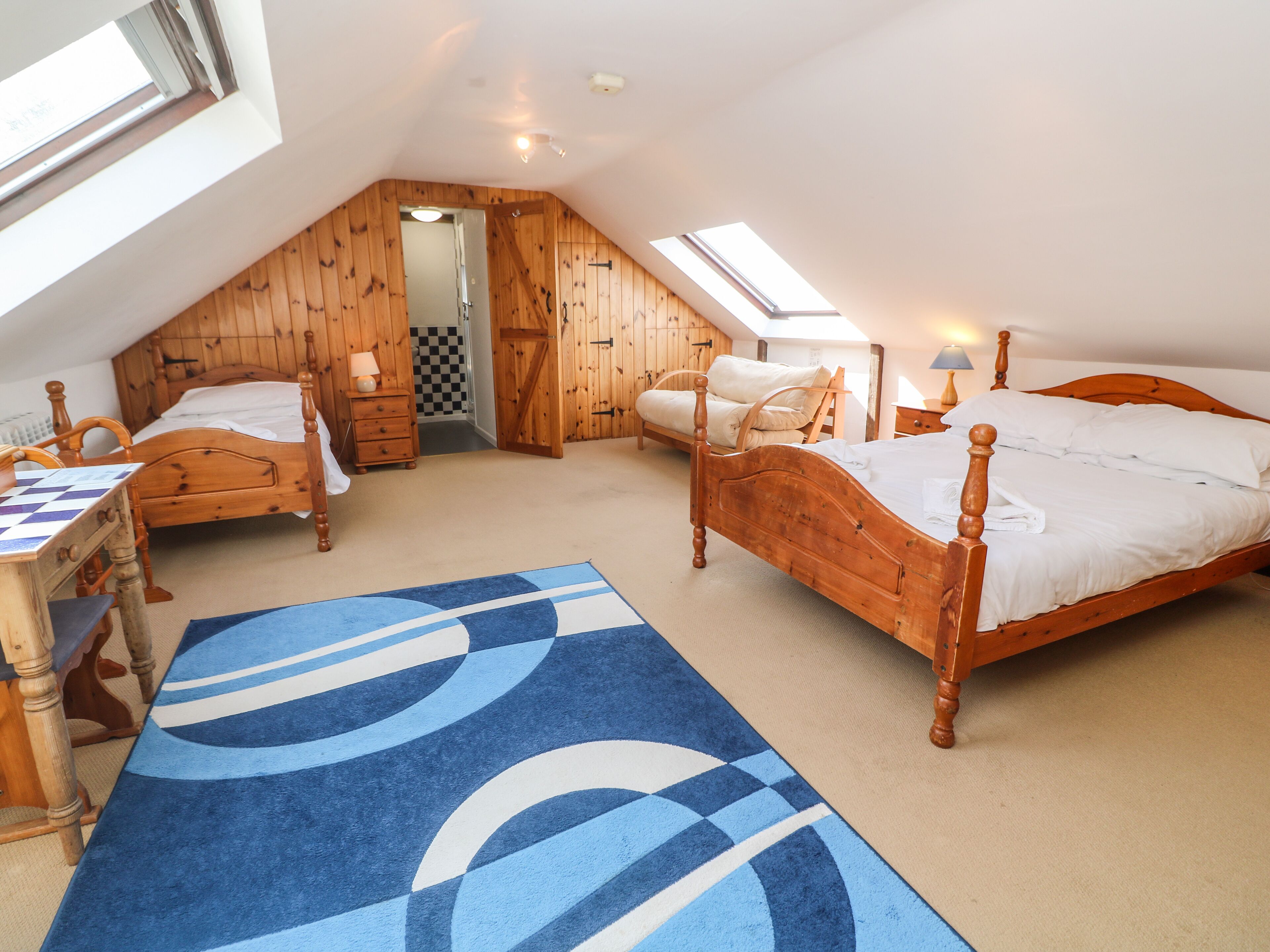 A cozy attic bedroom with two wooden beds, a desk, and a chair.