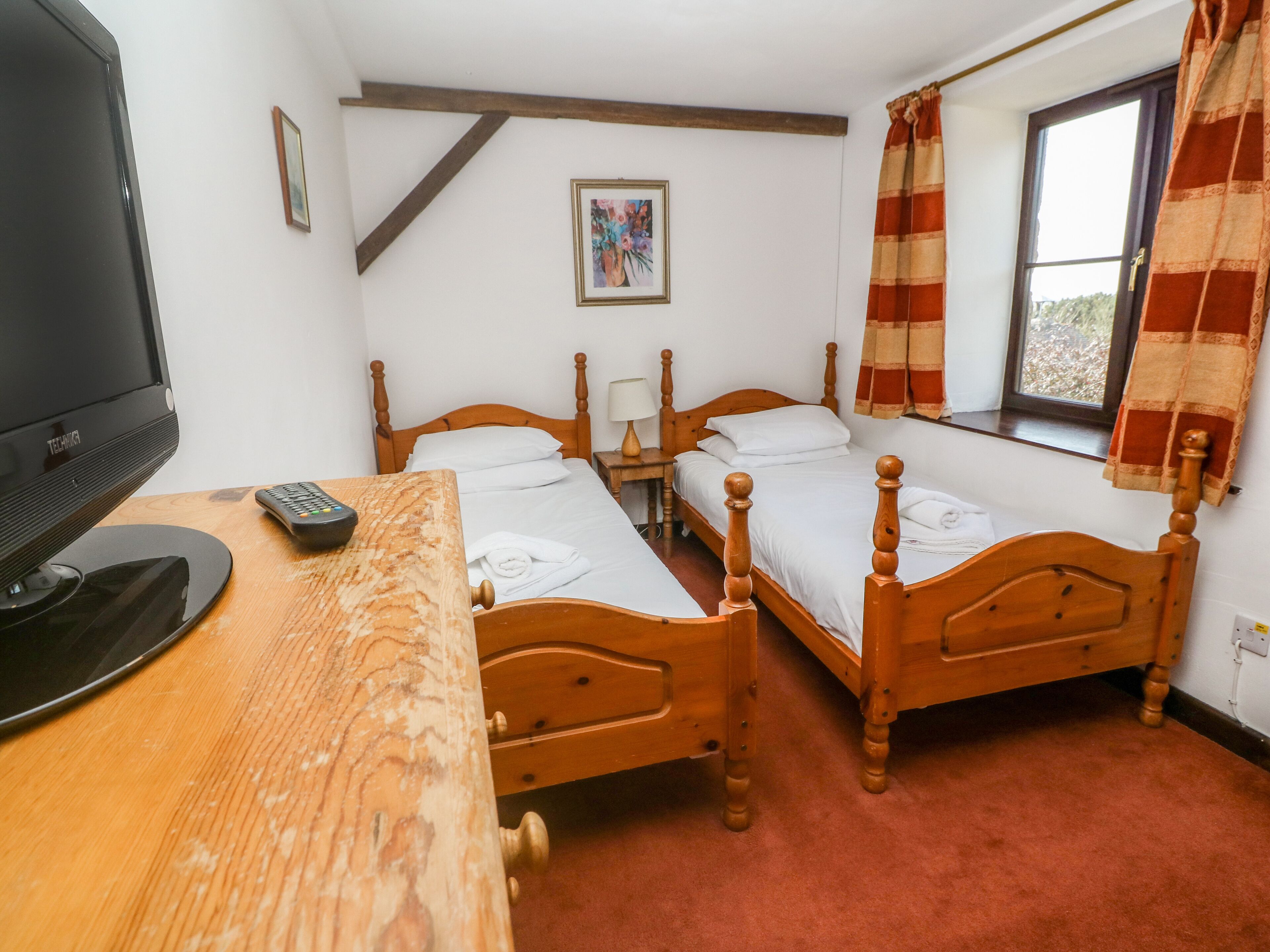 A room with two wooden beds, a TV, and a desk with a remote control.