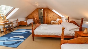 Una camera da letto mansardata accogliente, con soffitto a falde, pareti in legno, un grande letto con lenzuola bianche, una scrivania in legno e un tappeto blu con motivi.