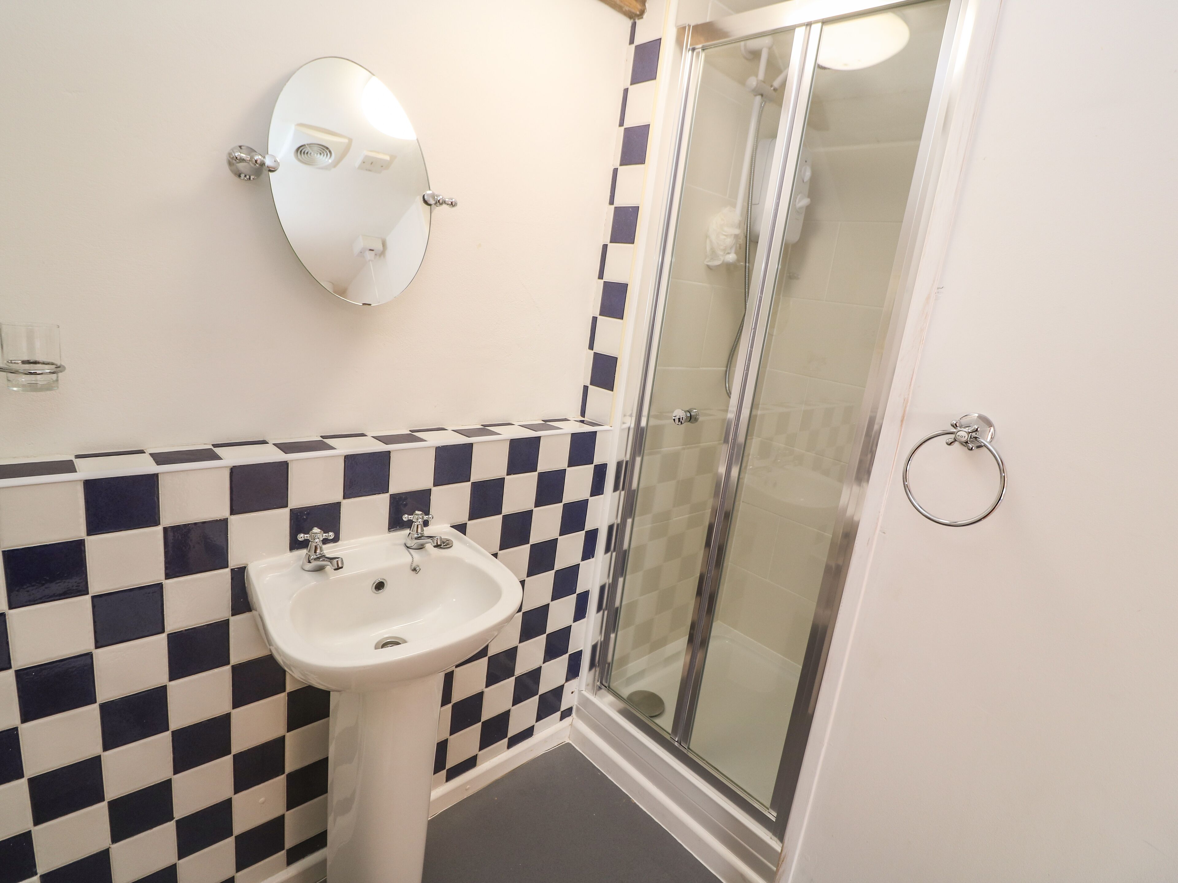 A bathroom with a checkered tile backsplash, a white sink, a mirror, and a glass shower enclosure.