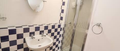 A bathroom with a checkered tile backsplash, a white sink, a mirror, and a glass shower enclosure.