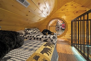 Um quarto de madeira aconchegante com uma janela redonda, uma cama com roupa de cama estampada e um urso de pelúcia.