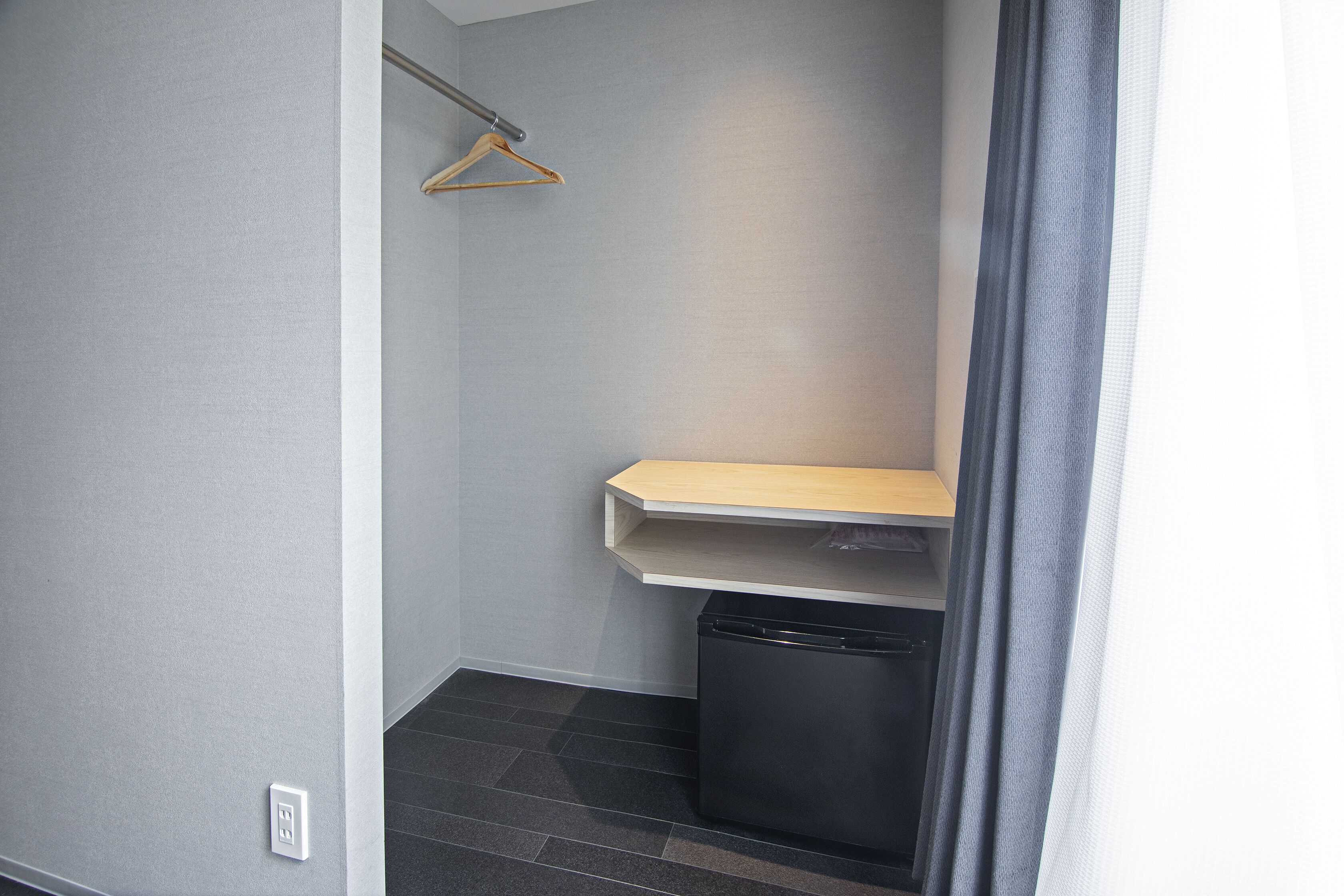 Une petite salle de bain fermée, avec une étagère en bois, une poubelle noire et un porte-serviettes.