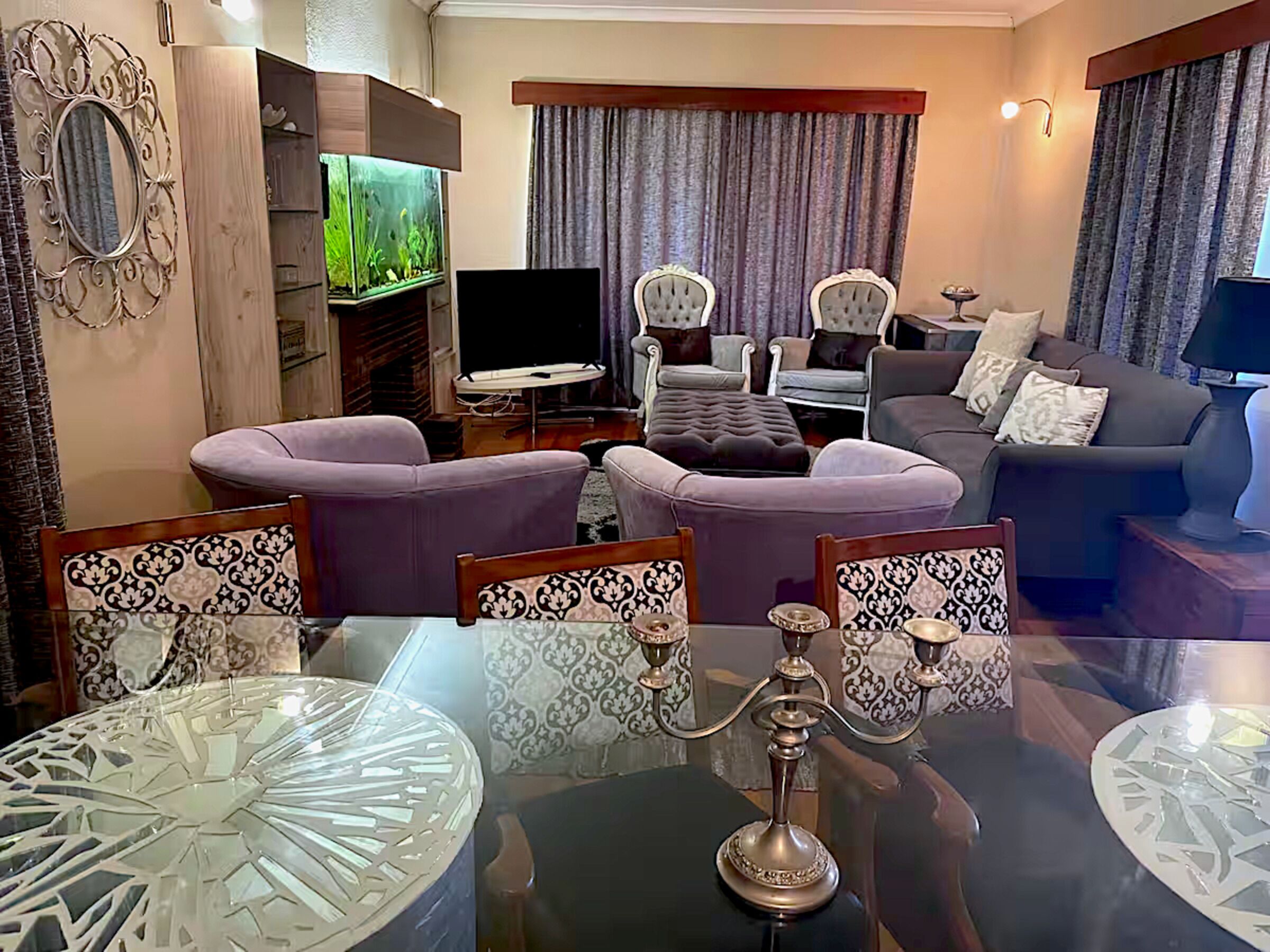 A modern living room with a glass coffee table, purple sofas, and a flat-screen TV.