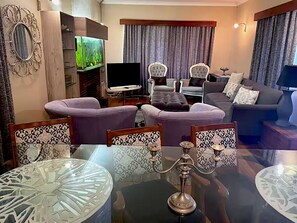 Ein modernes Wohnzimmer mit einem Glastisch, violetten Sofas und einem Flachbildfernseher.
