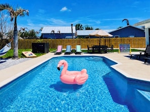 Una piscina con un flotador con forma de flamenco rosa, sillas de descanso y una cerca de madera.