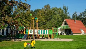 Ein Spielplatz mit verschiedenen Spielgeräten, einem kleinen Gebäude mit rotem Dach und einer Rasenfläche.