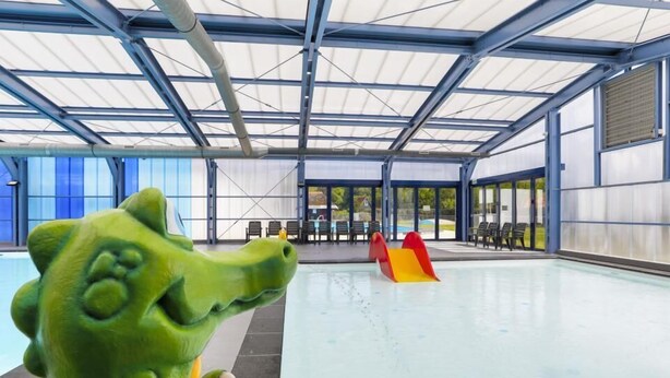 Ein Schwimmbeckenbereich mit überdachtem Bereich, einer Rutsche und einer großen, grünen Skulptur.