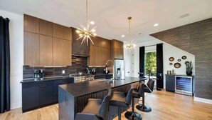 Una cocina moderna con armarios oscuros, una isla central con taburetes y luces colgantes.