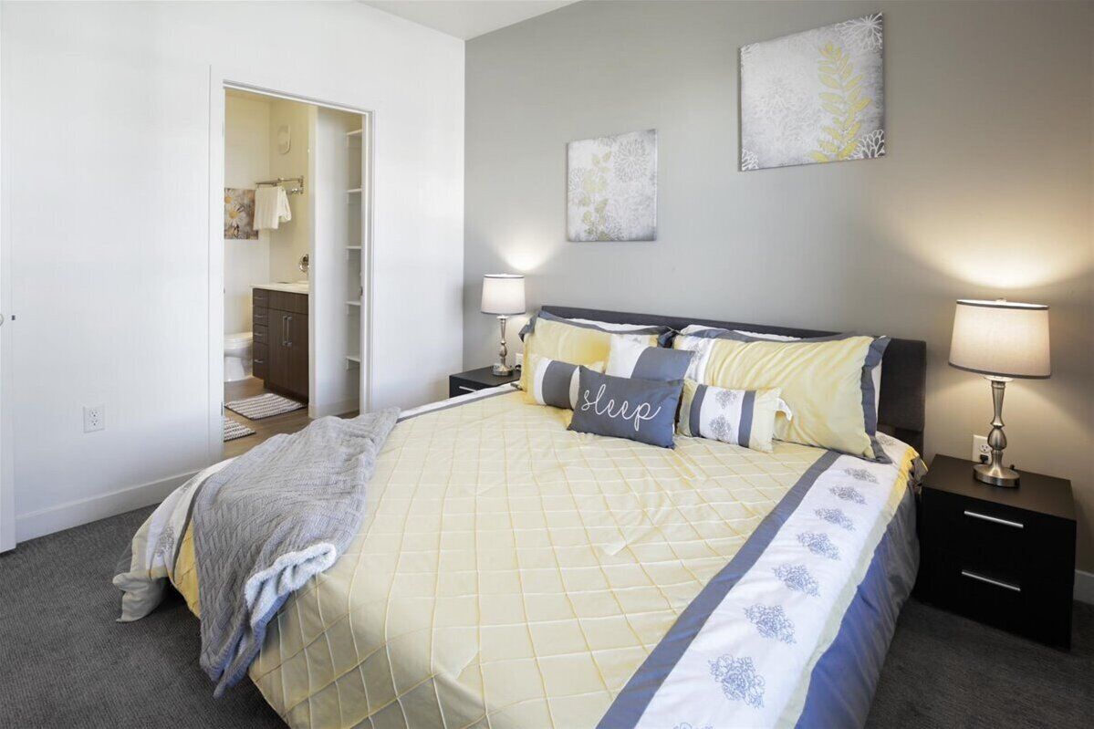 A bedroom with a bed, bedside tables, a nightstand, a wardrobe, and a door leading to a bathroom.