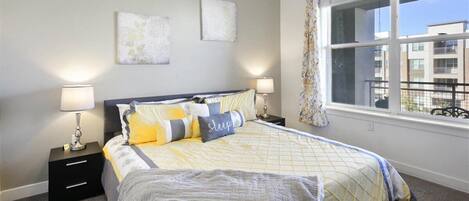A bedroom with a bed, two bedside tables, a window with a view, and two wall-mounted lamps.