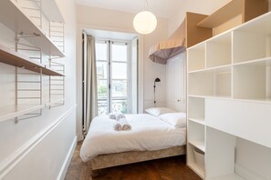 A bedroom with a bed, a wardrobe, a hanging light, and a window with curtains.