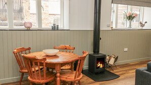 A dining area with a round wooden table and chairs, a black wood-burning stove, and a window with a view of the outside. - The Bakery (Belford)