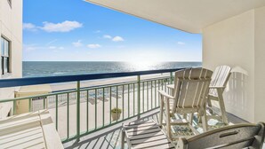 Un balcon avec vue sur l’océan, deux fauteuils Adirondack, une petite table et un panneau indiquant : « RÈGLES DE LA PISCINE ».