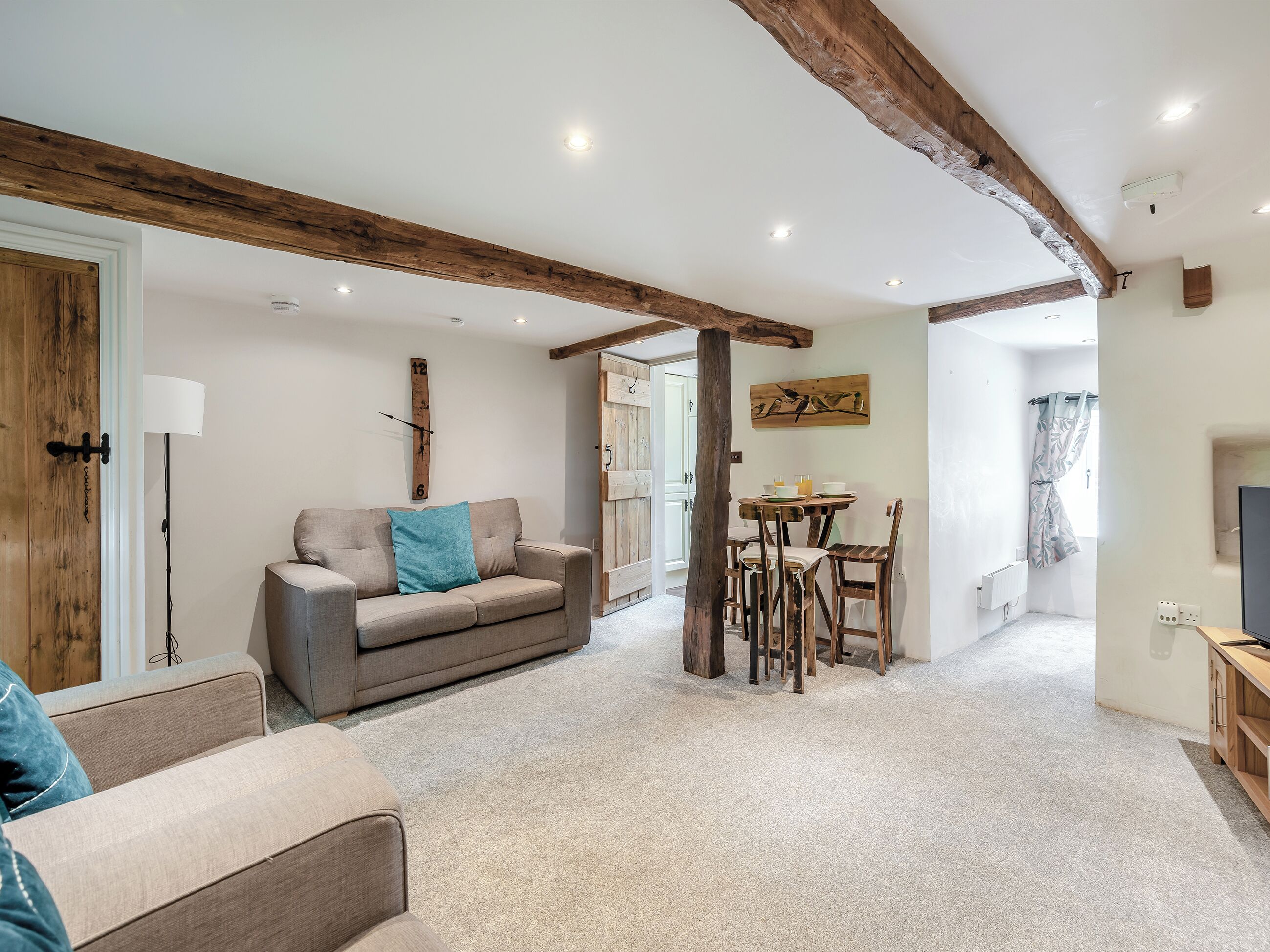 Un salon avec un canapé, une table à manger et des chaises, une poutre en bois au plafond et une horloge au mur.