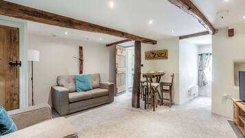 Un salon avec un canapé, une table à manger et des chaises, une poutre en bois au plafond et une horloge au mur.