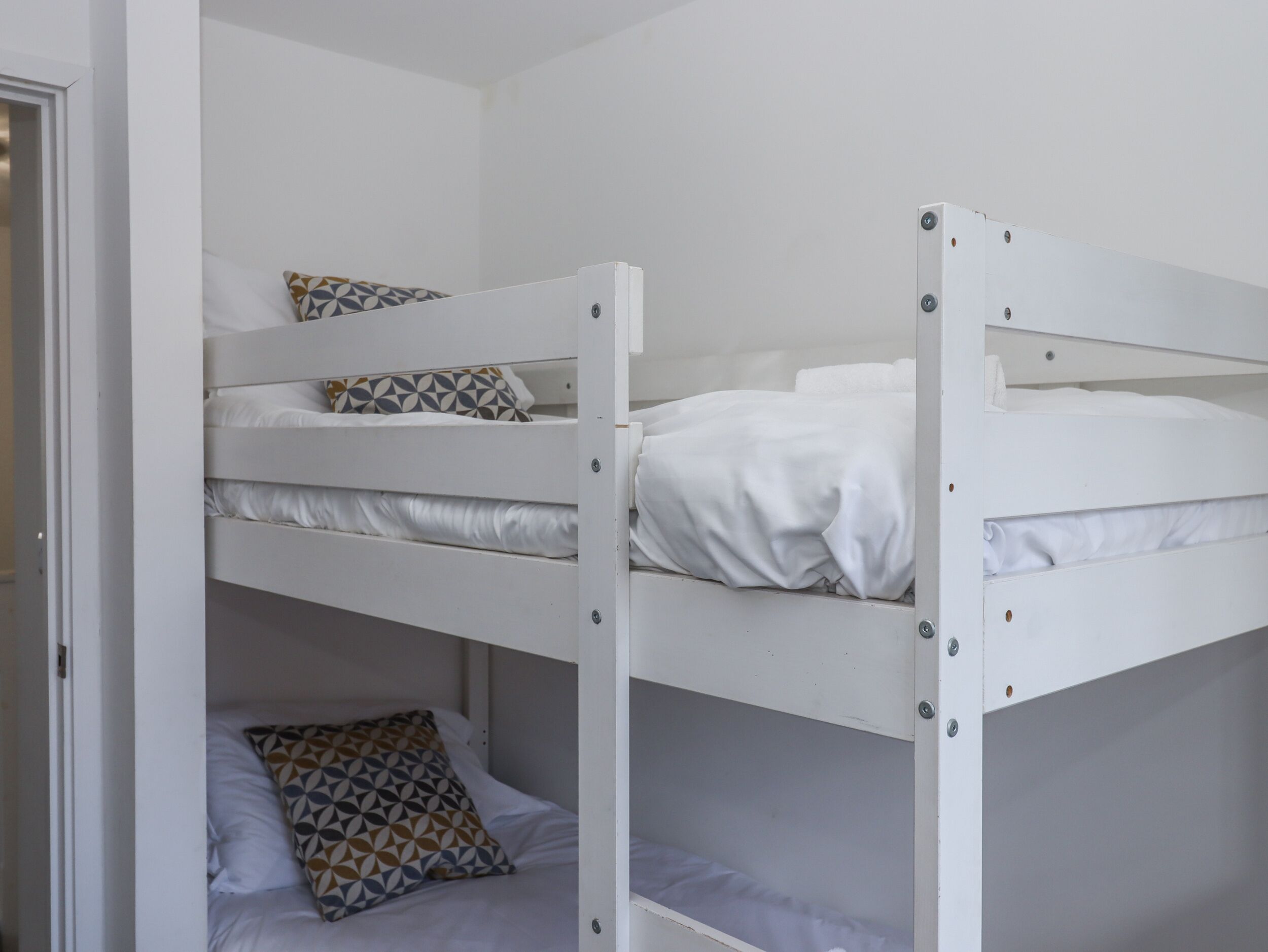 A bunk bed room with white bedding and patterned pillows.