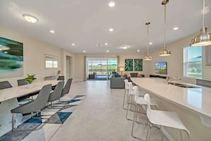 A modern kitchen with a large island, bar stools, and pendant lighting.