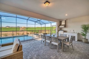 A covered patio with a pool, outdoor seating, and a kitchen area.