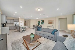 A modern living space with a kitchen, dining area, and a gray sofa with patterned cushions.