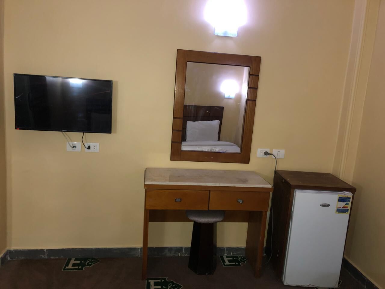A small room with a wooden desk, a mirror, a television, and a refrigerator.