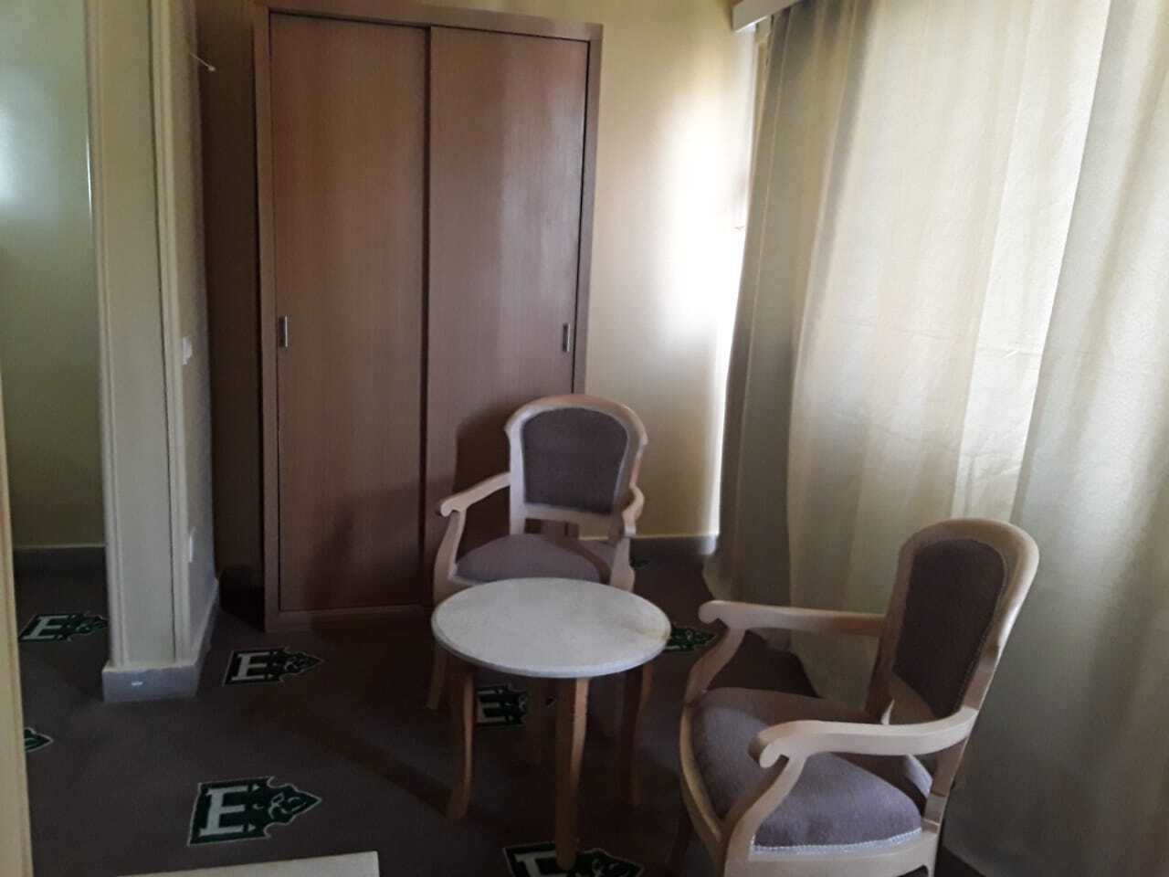A small room with a wooden wardrobe, two wooden chairs, and a round table.