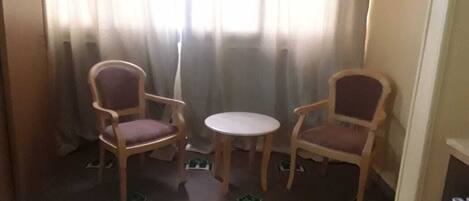 A hotel room with a bed, two wooden chairs, a small round table, and a window with curtains.