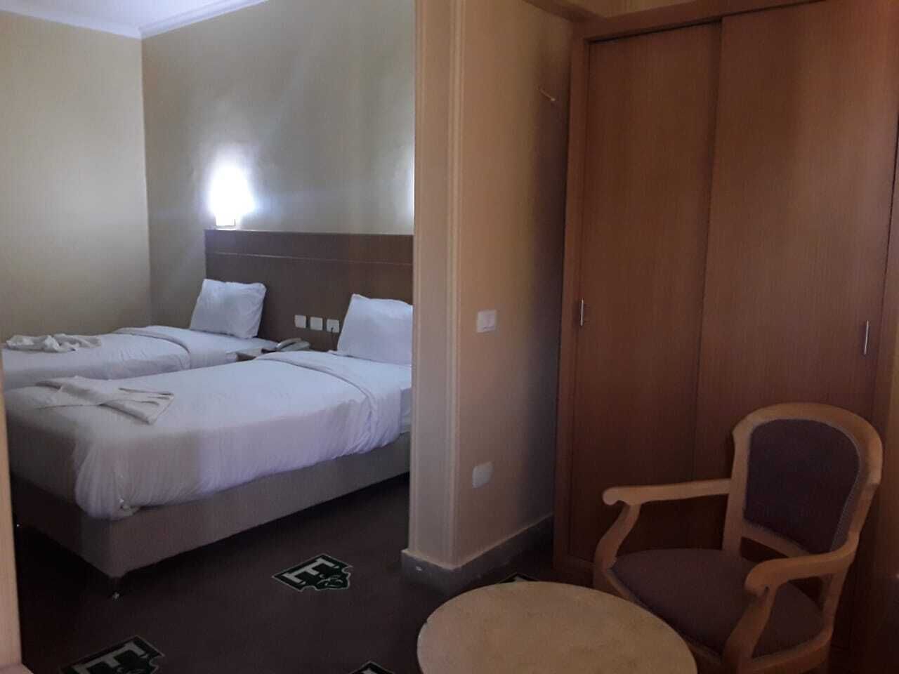 Une chambre d’hôtel avec deux lits, une armoire en bois et une seule chaise.