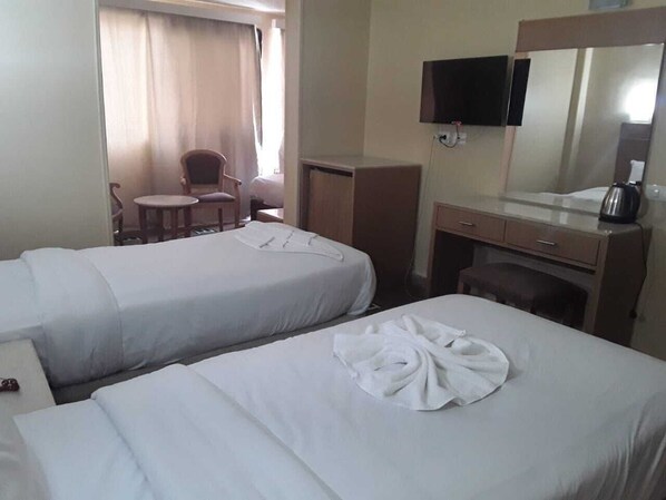 A hotel room with two beds, a desk, a chair, a television, and a mirror. - Regency Hotel (Giza)