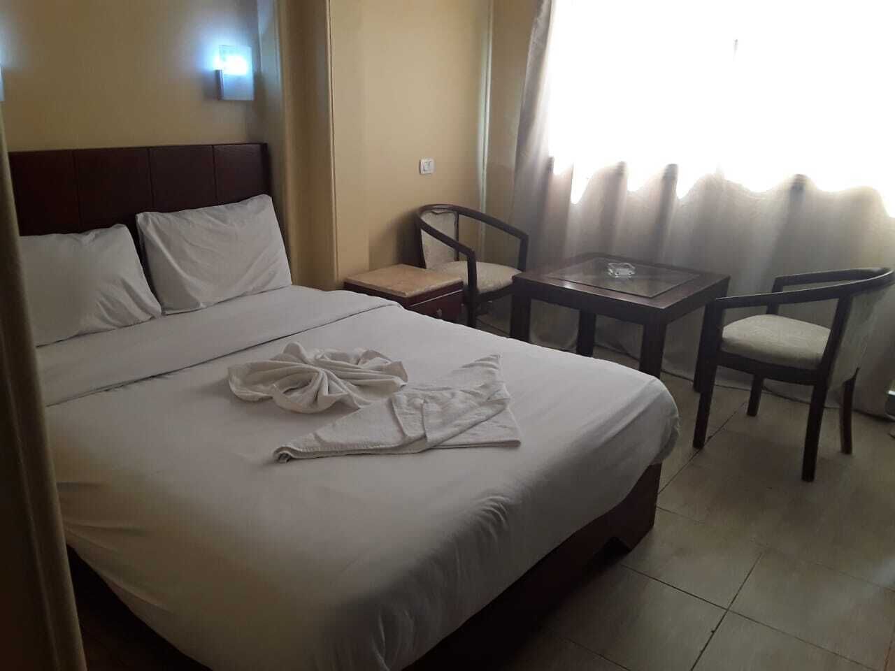 A hotel room with a bed, two chairs, a small table, and a window with curtains.
