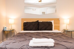 Un lit bien fait, avec une tête de lit et des oreillers de couleur marron foncé, deux lampes de chevet et un miroir au-dessus du lit.