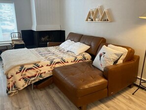 A bedroom with a bed, a brown leather sofa, a fireplace, and a wall-mounted shelf.