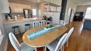 Una cocina moderna con armarios blancos, un refrigerador de acero inoxidable y una mesa de comedor de madera con sillas blancas.