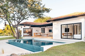 A modern house with a swimming pool, a dining area, and a large sliding glass door leading to a living room.