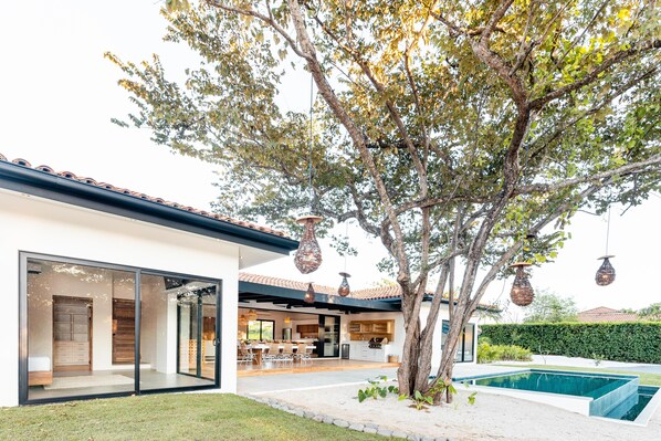 A modern house with a large glass door, a dining area, and a swimming pool.
