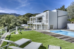 Une maison moderne à deux étages, dotée d’une piscine, d’un espace extérieur aménagé et couvert, et d’une pelouse bien entretenue.