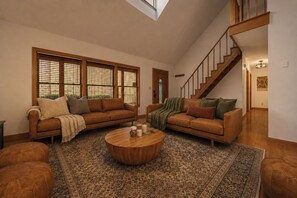 Un salón amplio con dos sofás de cuero, una mesa de centro de madera y una escalera.