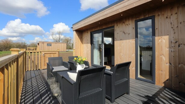A wooden deck with outdoor furniture and a glass door leading to an interior space. - The Wren (Whitchurch)