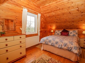 Un dormitorio rústico de cabaña de madera con cama, cómoda, ventana y dos lámparas de noche.