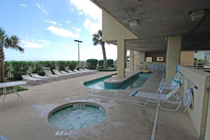 Uma área de piscina com espreguiçadeiras, uma banheira de hidromassagem e vista para o oceano.