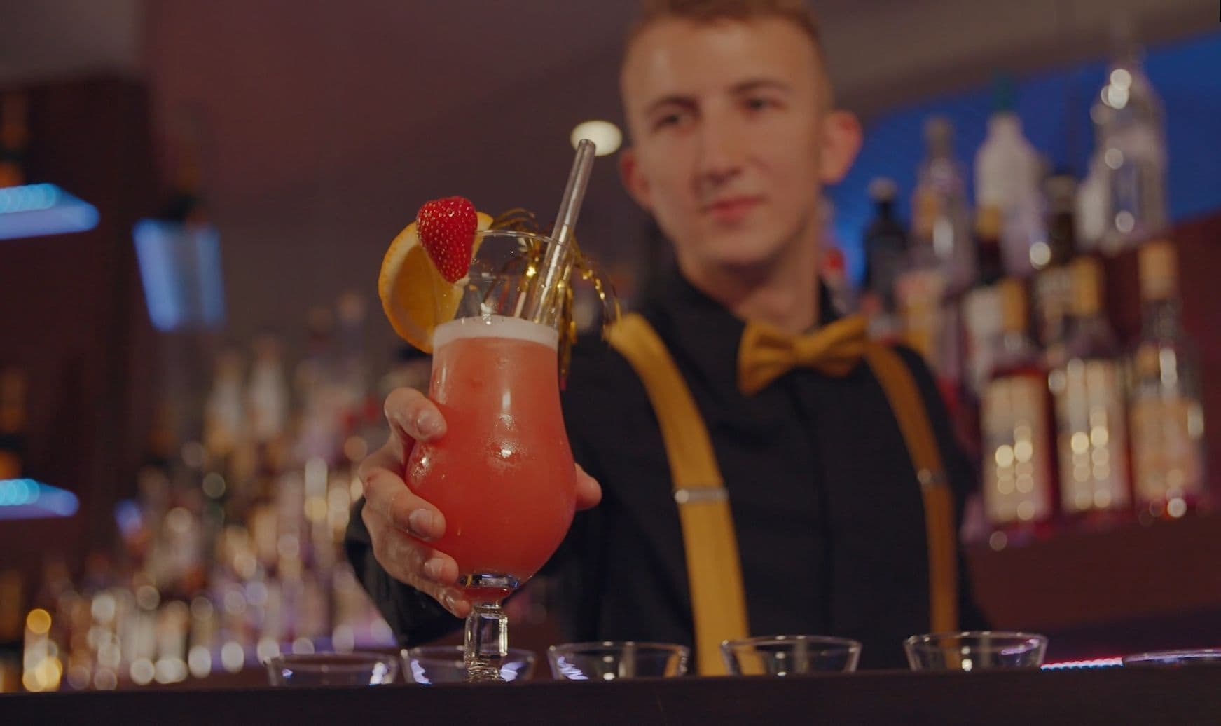 A bartender holding a cocktail with a strawberry garnish.