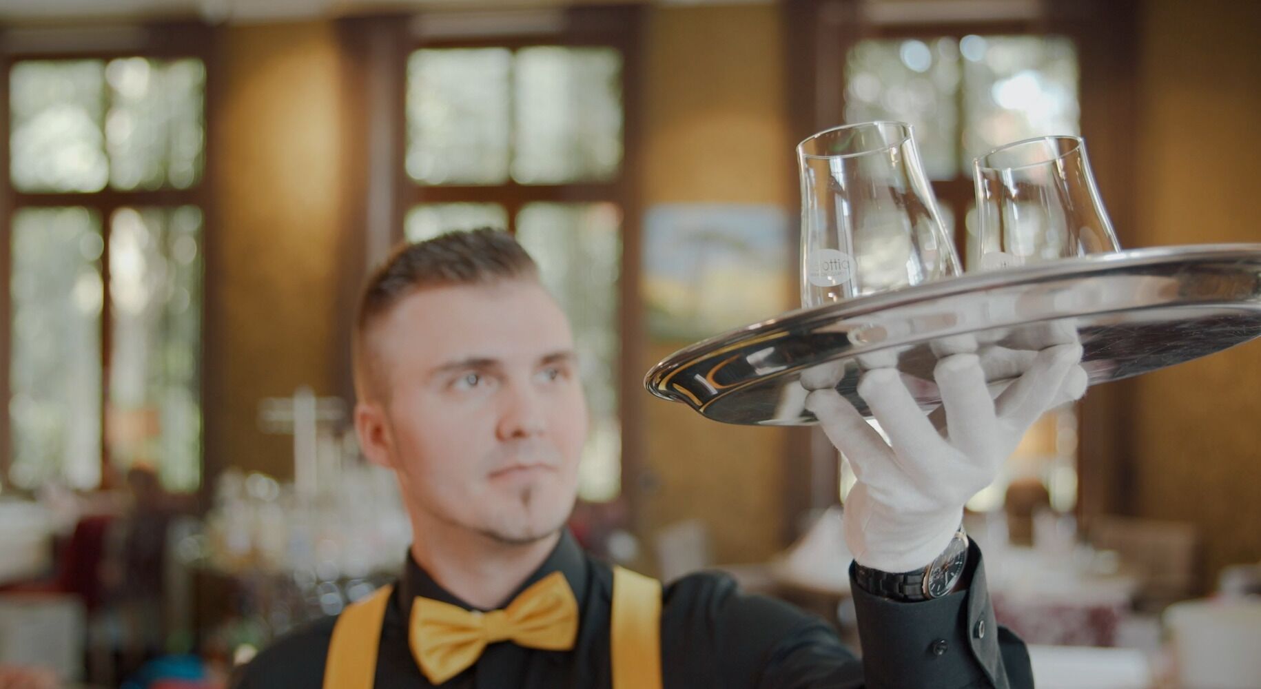 A waiter holding a tray with glasses and a bottle, likely in a restaurant setting.