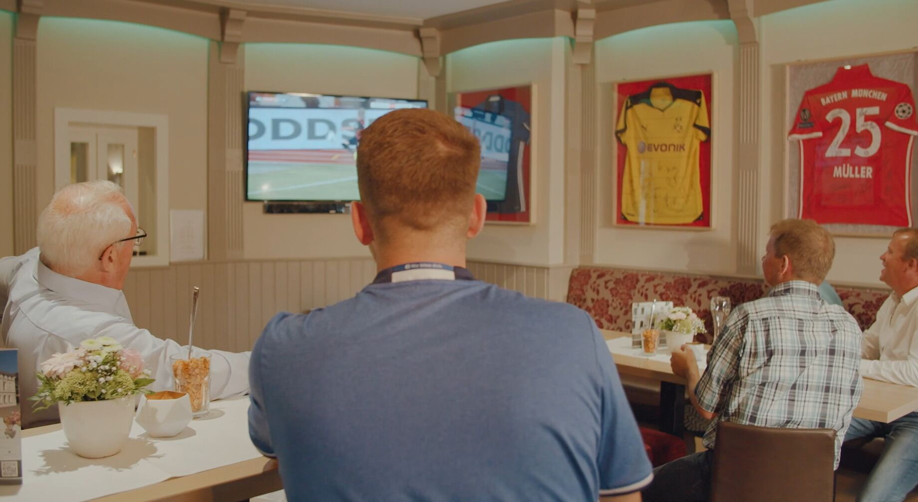 Un groupe de personnes est assis à une table dans un restaurant, devant un téléviseur qui diffuse un événement sportif.