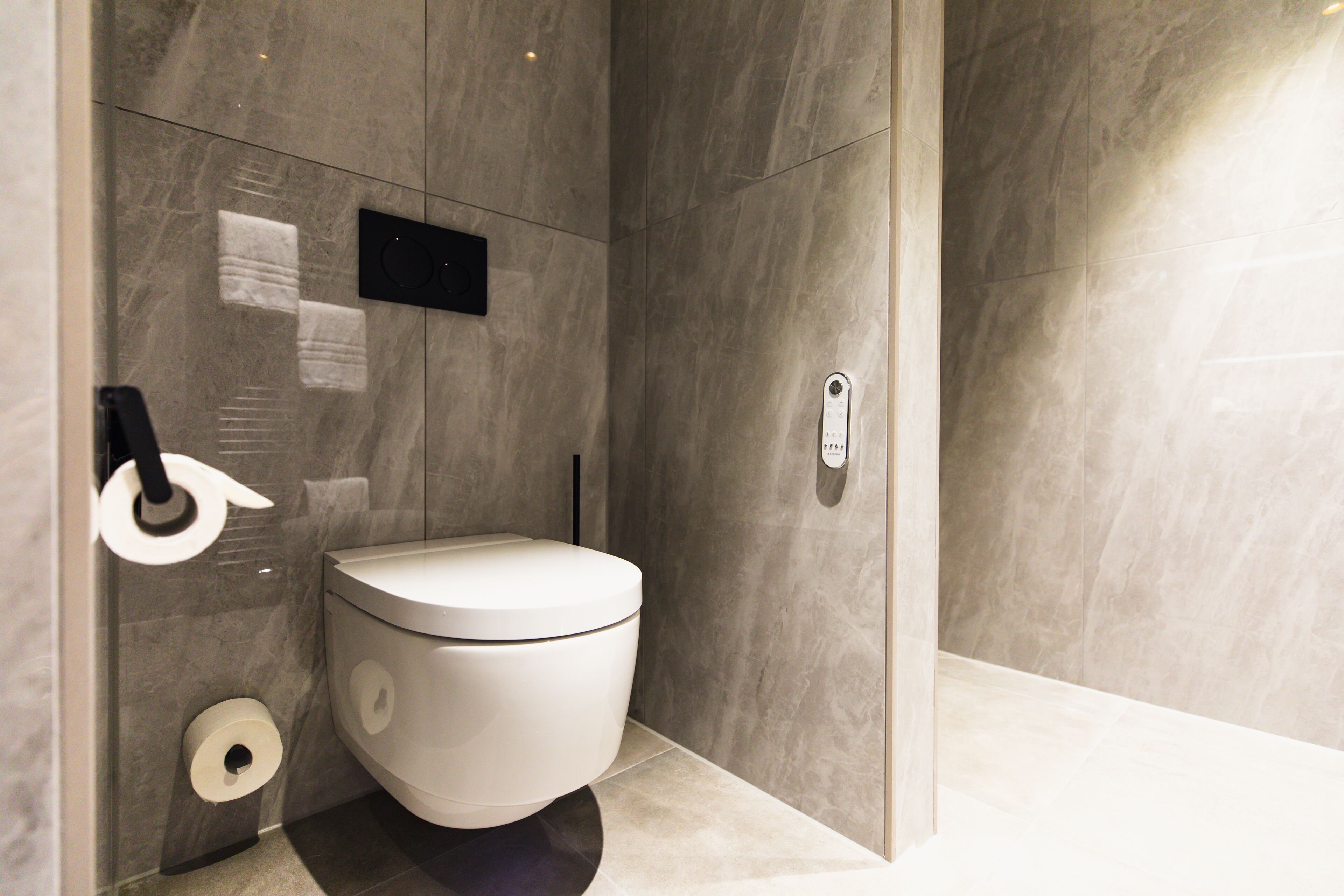 A modern bathroom with a toilet, marble walls, and a glass shower enclosure.